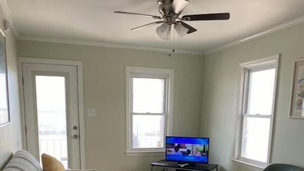 A living room with a grey sofa, a wooden coffee table, a television on a stand, a black chair, and a ceiling fan. - Rio Motel and Suites (Wildwood)