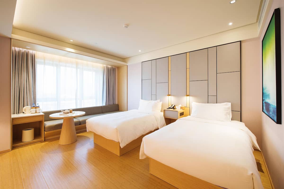 A hotel room with two beds, a sofa, a round table, and a large window with curtains.