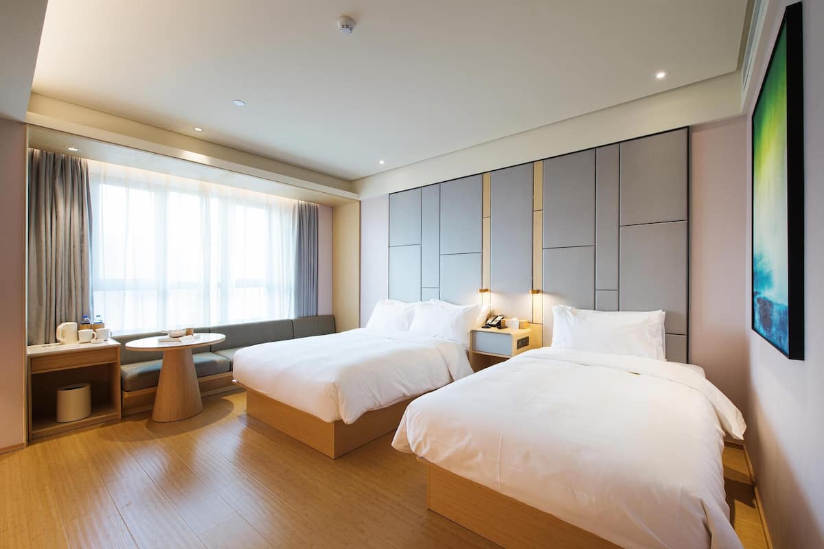 A hotel room with two beds, a sofa, a small table, a nightstand, and a large window with curtains.