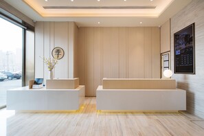 A modern reception area with a wooden panel wall, a reception desk, a vase with flowers, and a digital display.