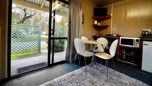 Quarto com porta de vidro deslizante para um pátio, uma pequena mesa de jantar com cadeiras, micro-ondas e frigorífico.