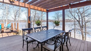 A covered outdoor patio with a table and chairs, overlooking a body of water and trees. - Lake front with dock and boat ramp (Waverly)