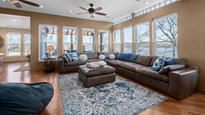 A spacious living room with a large sectional sofa, a ceiling fan, and large windows providing natural light. - Lake front with dock and boat ramp (Waverly)