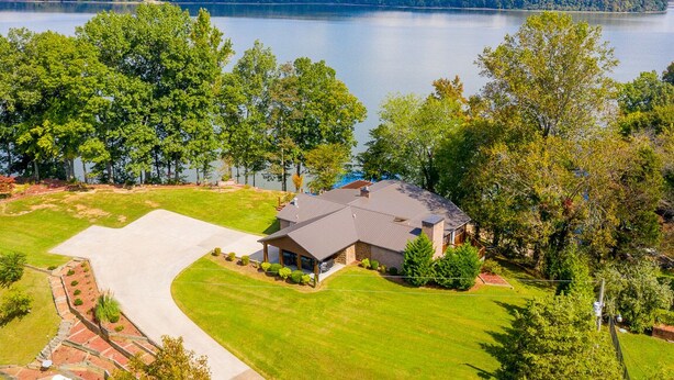 A house with a large driveway, a well-maintained lawn, and a view of a lake and hills in the background. - Lake front with dock and boat ramp (Waverly)