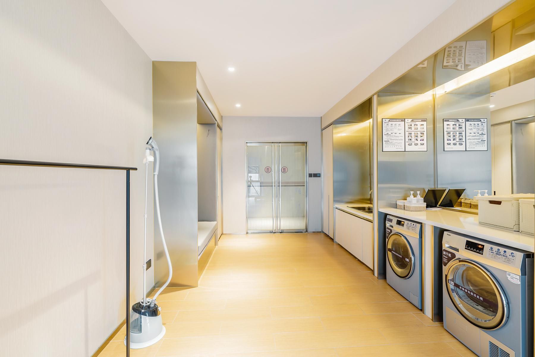 Una habitación de hotel moderna con un pasillo que conduce a una puerta, una aspiradora y una lavadora.