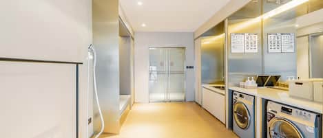 A modern hotel room with a hallway leading to a door, a vacuum cleaner, and a washing machine.