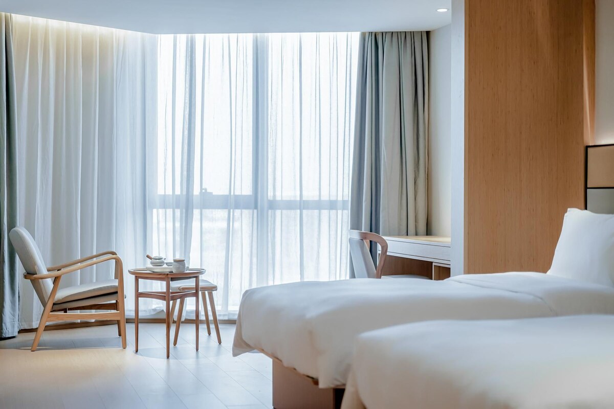 Quarto de hotel com uma cama, uma mesa de escritório, uma cadeira e uma pequena mesa com um bule de chá.