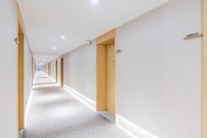 Corredor longo e estreito em um hotel, com portas de madeira e piso coberto por carpete.