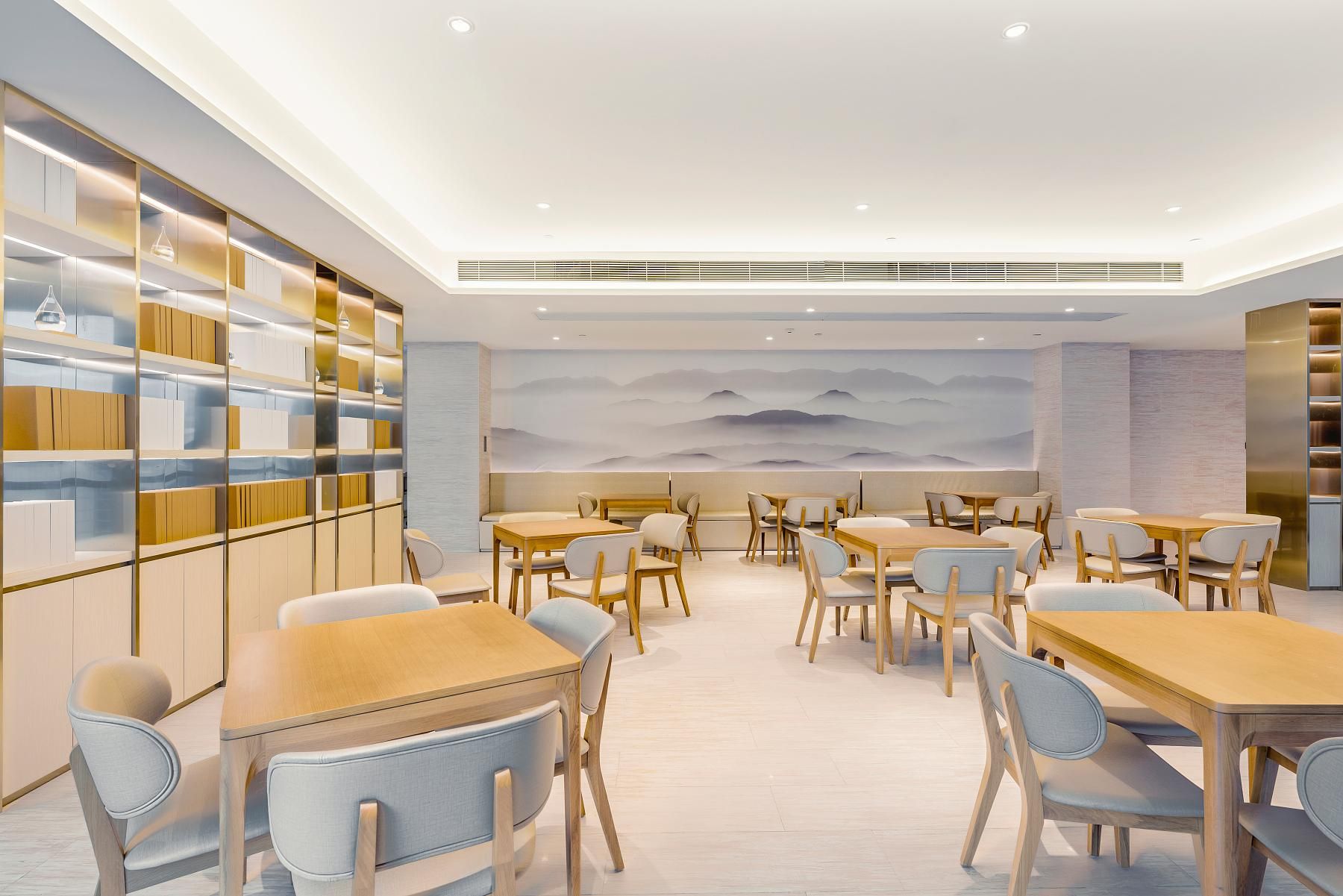 A modern dining area with tables and chairs, a bookshelf, and a mural on the wall.