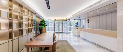 A modern hotel lobby with a long reception desk, a turnstile entrance, and a large potted plant.