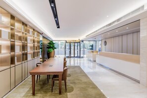 Un vestíbulo de hotel moderno con un mostrador de recepción alargado, un torniquete de acceso y una planta grande en maceta.