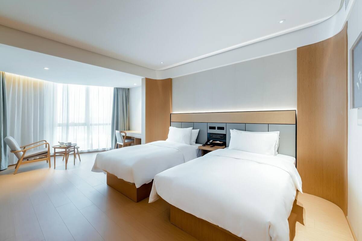 Une chambre d’hôtel avec deux lits, un bureau, une chaise et une grande fenêtre avec des rideaux.