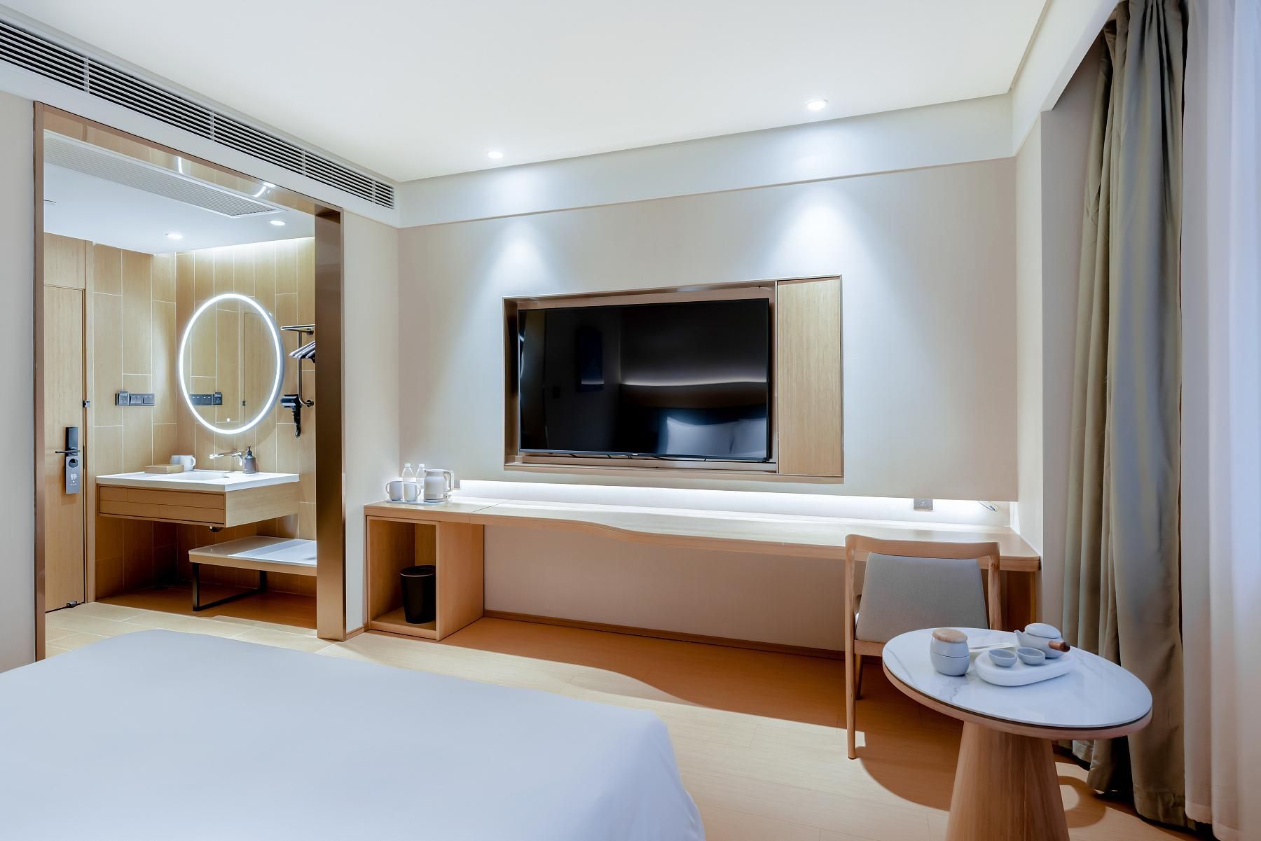 Una habitación de hotel con una cama, un escritorio con televisor, un espejo y una mesita con tazas.