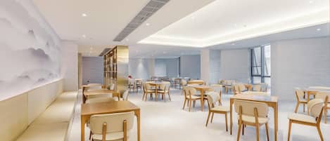 A modern dining area with wooden tables and chairs, a decorative wall with a mountain design, and a large window providing natural light.