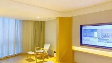 Una habitación de hotel con cama, escritorio, silla, televisor y ventana con cortinas.