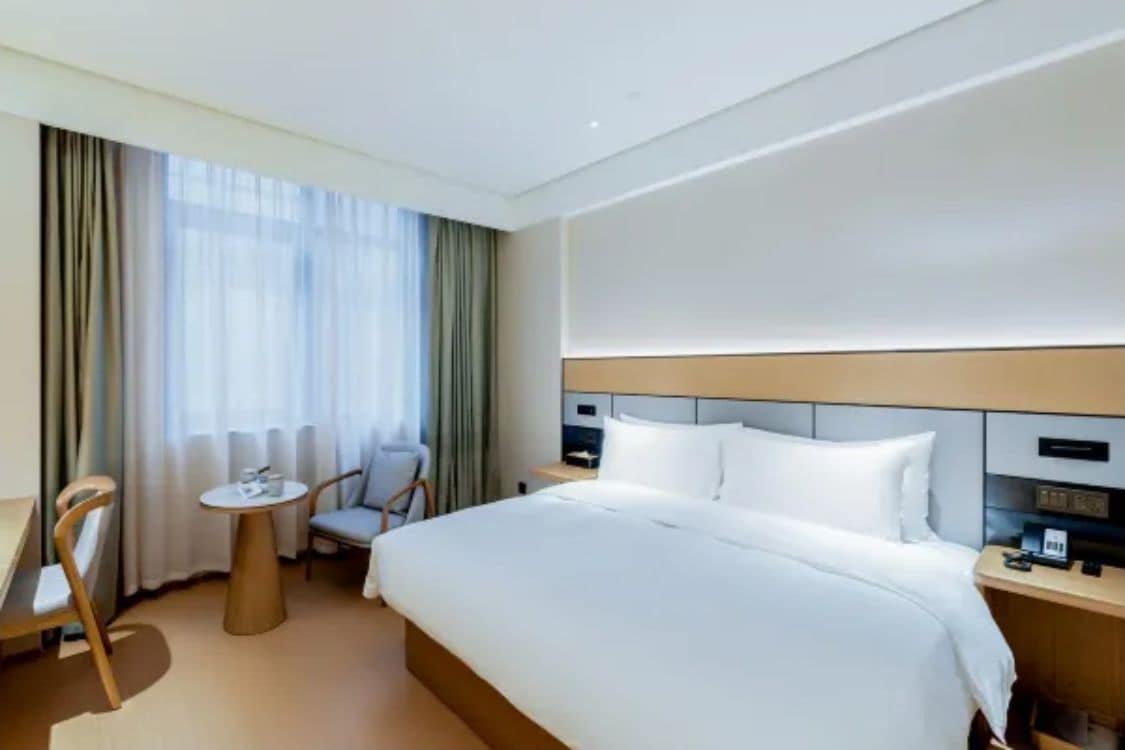 A hotel room with a bed, a desk, a chair, and a window with curtains.