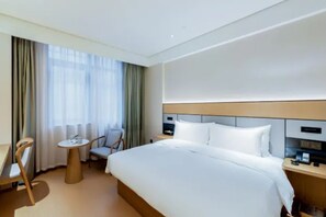 Una habitación de hotel con cama, escritorio, silla y ventana con cortinas.