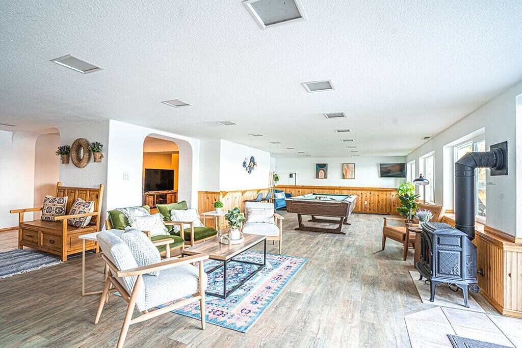 A spacious living room with a pool table, comfortable seating, and a wood-burning stove.