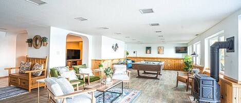 A spacious living room with a pool table, comfortable seating, and a wood-burning stove.