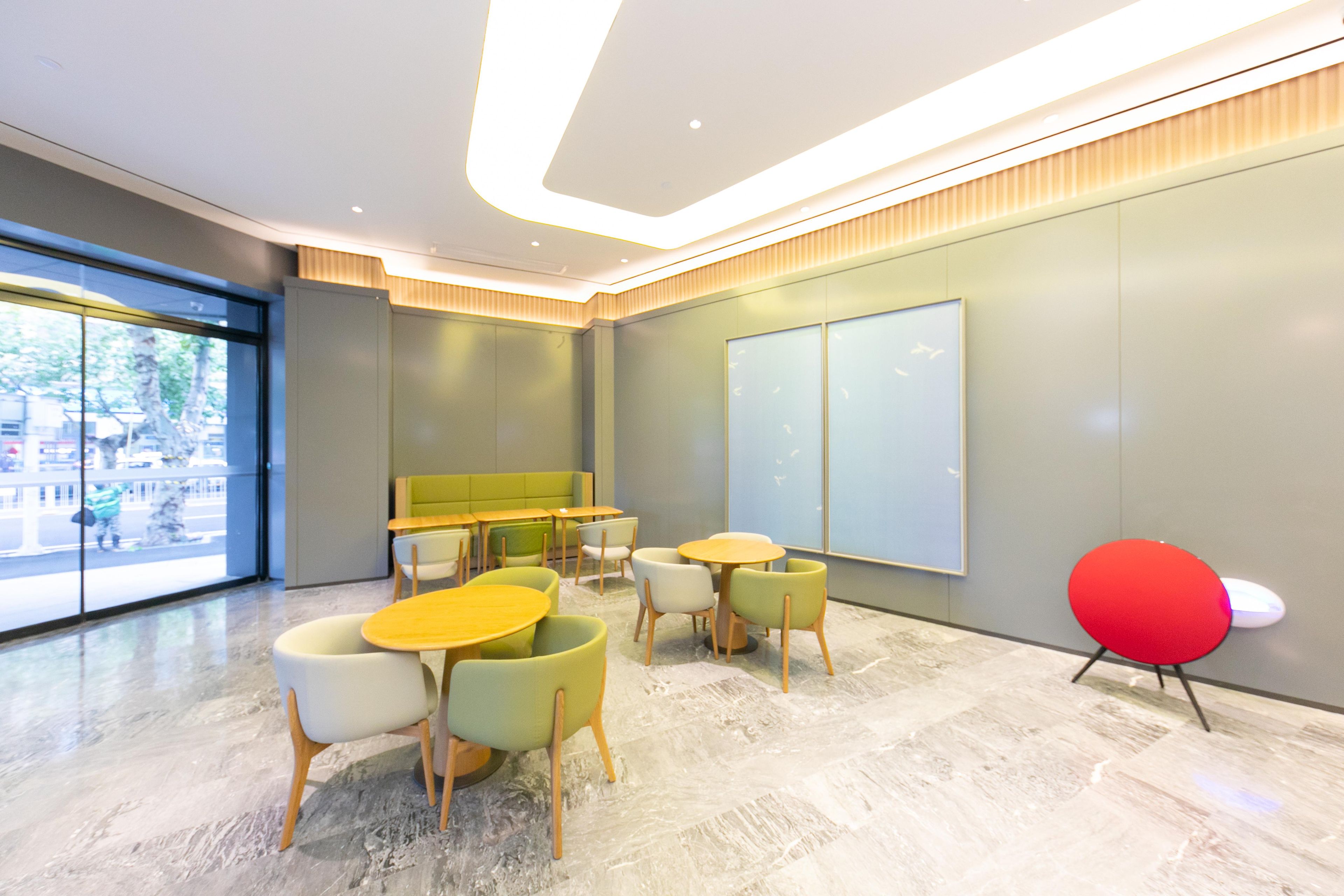 Een modern interieur met een zithoek met ronde tafels en stoelen, een groot raam met uitzicht op de straat en een rode accentstoel.