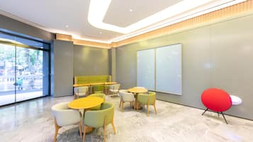 Een modern interieur met een zithoek met ronde tafels en stoelen, een groot raam met uitzicht op de straat en een rode accentstoel.