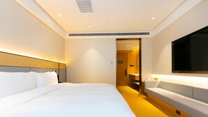 Une chambre d’hôtel avec un grand lit, une table de chevet, une télévision et une salle de bain visible à travers une porte ouverte.
