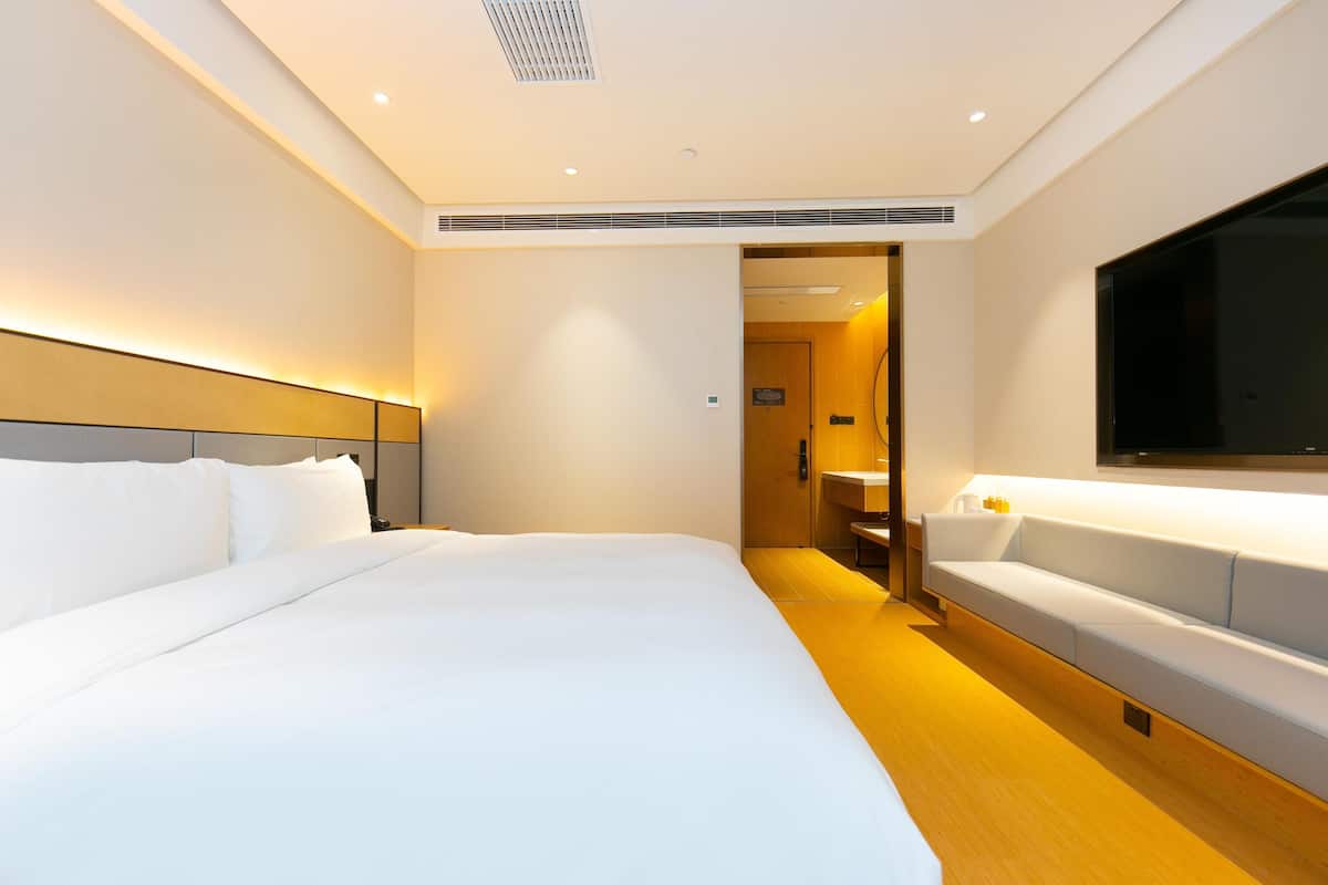 A hotel room with a large bed, a bedside table, a TV, and a bathroom visible through an open door.
