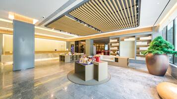 A modern lobby with a reception desk, seating area, and a large potted plant.