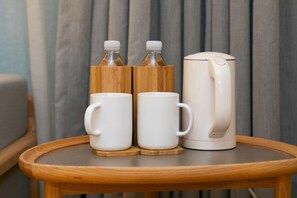 Una mesa de madera con dos tazas blancas y una tetera eléctrica blanca.
