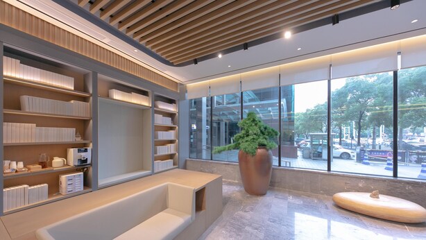 Un hall d’entrée moderne avec un espace salon, une grande plante en pot et une vue sur la rue grâce à de grandes fenêtres.