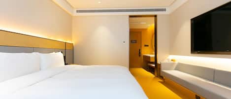A hotel room with a large bed, a bedside table, a TV, and a bathroom visible through an open door.