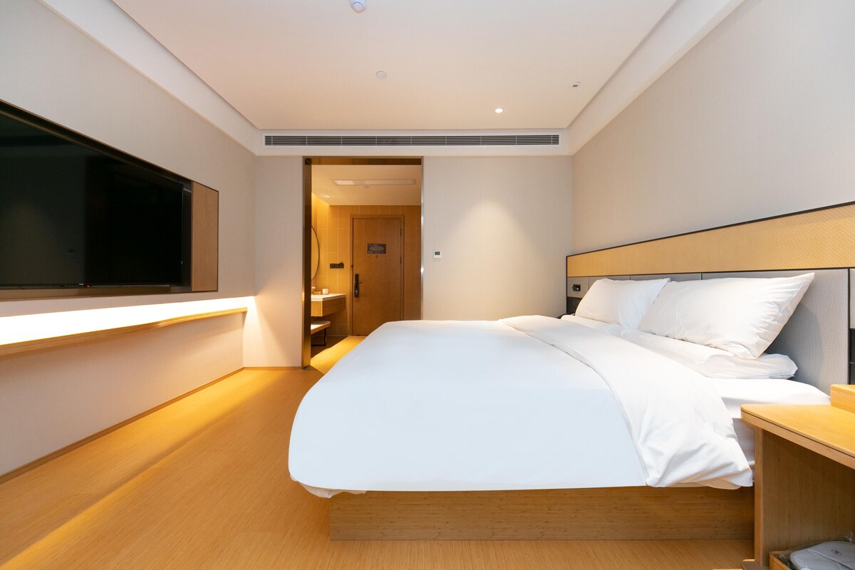 A modern hotel room with a large bed, bedside table, and a flat-screen TV mounted on the wall.