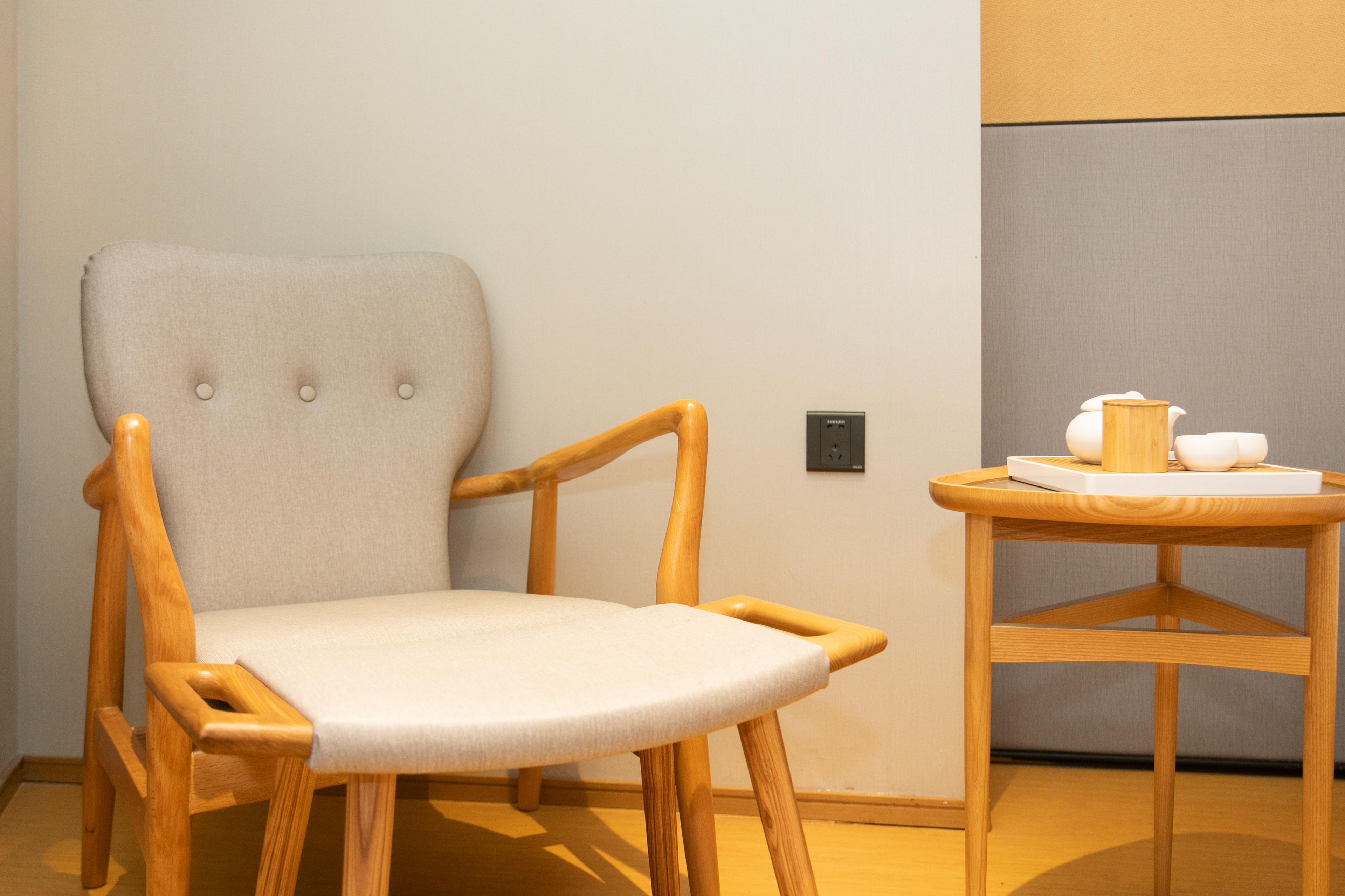 Una silla de madera con asiento y respaldo acolchados, ubicada junto a una pequeña mesa de madera que sostiene una bandeja con una tetera y tazas.