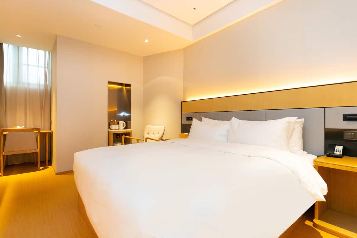 A modern hotel room with a large bed, bedside tables, a chair, and a mirror.