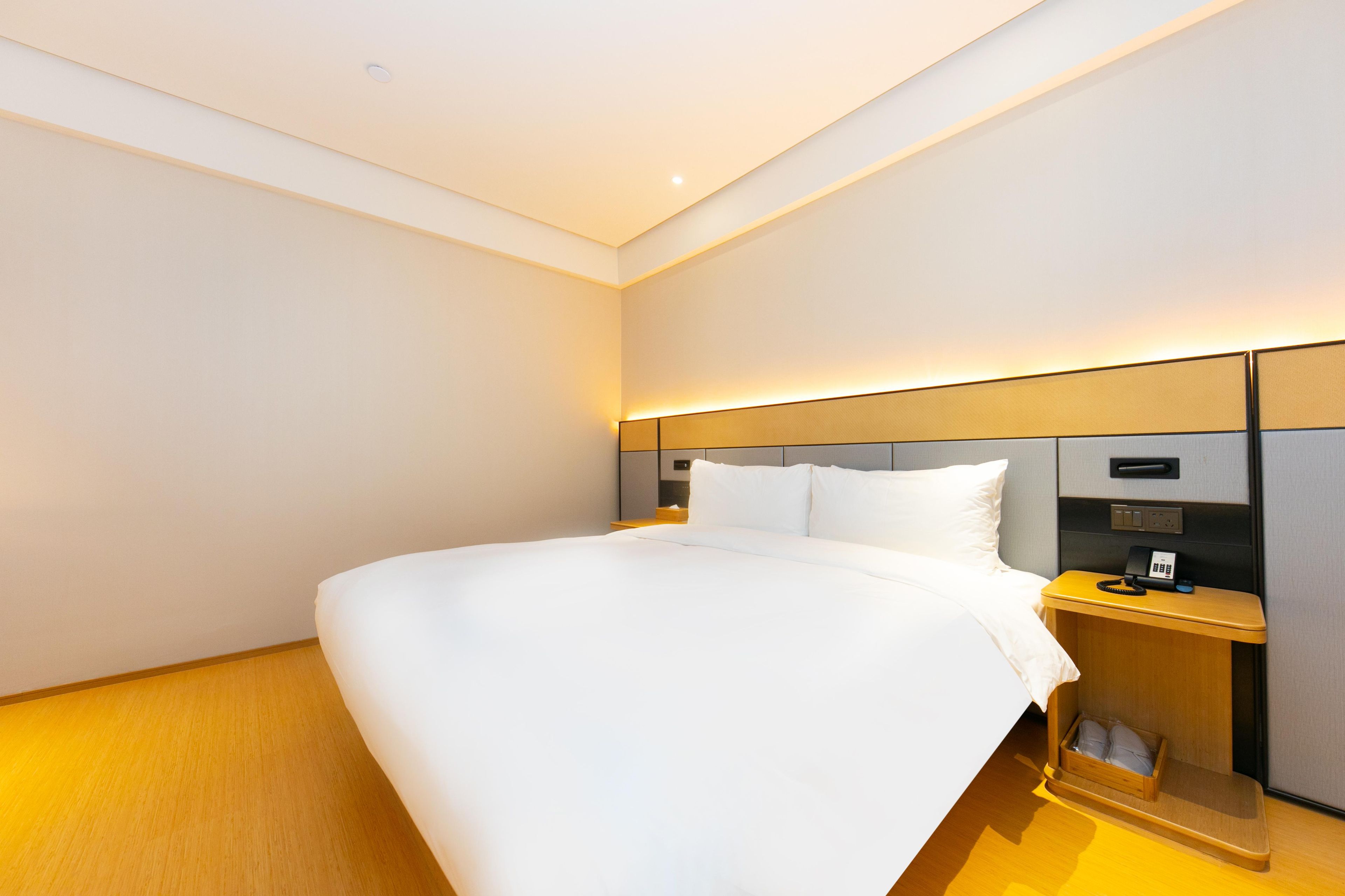A modern hotel room with a large bed, bedside tables, and a built-in nightstand.