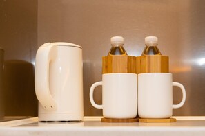 A white electric kettle and two white mugs with wooden handles on a countertop. - Ji Hotel (Wuhan)