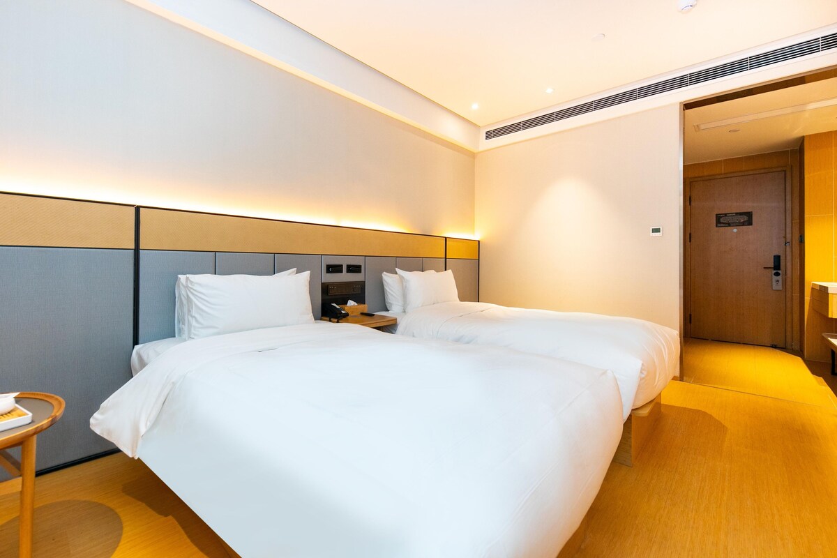 A hotel room with two beds, a bedside table with a phone, and a door leading to a bathroom.