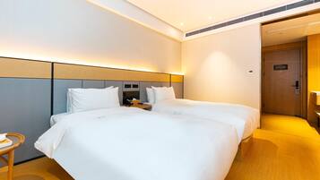 A hotel room with two beds, a bedside table with a phone, and a door leading to a bathroom.