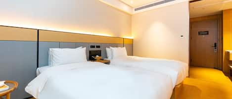 A hotel room with two beds, a bedside table with a phone, and a door leading to a bathroom.