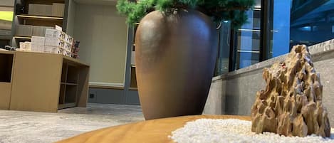 A reception area with a large potted plant, a wooden table with a decorative rock, and a counter with boxes.