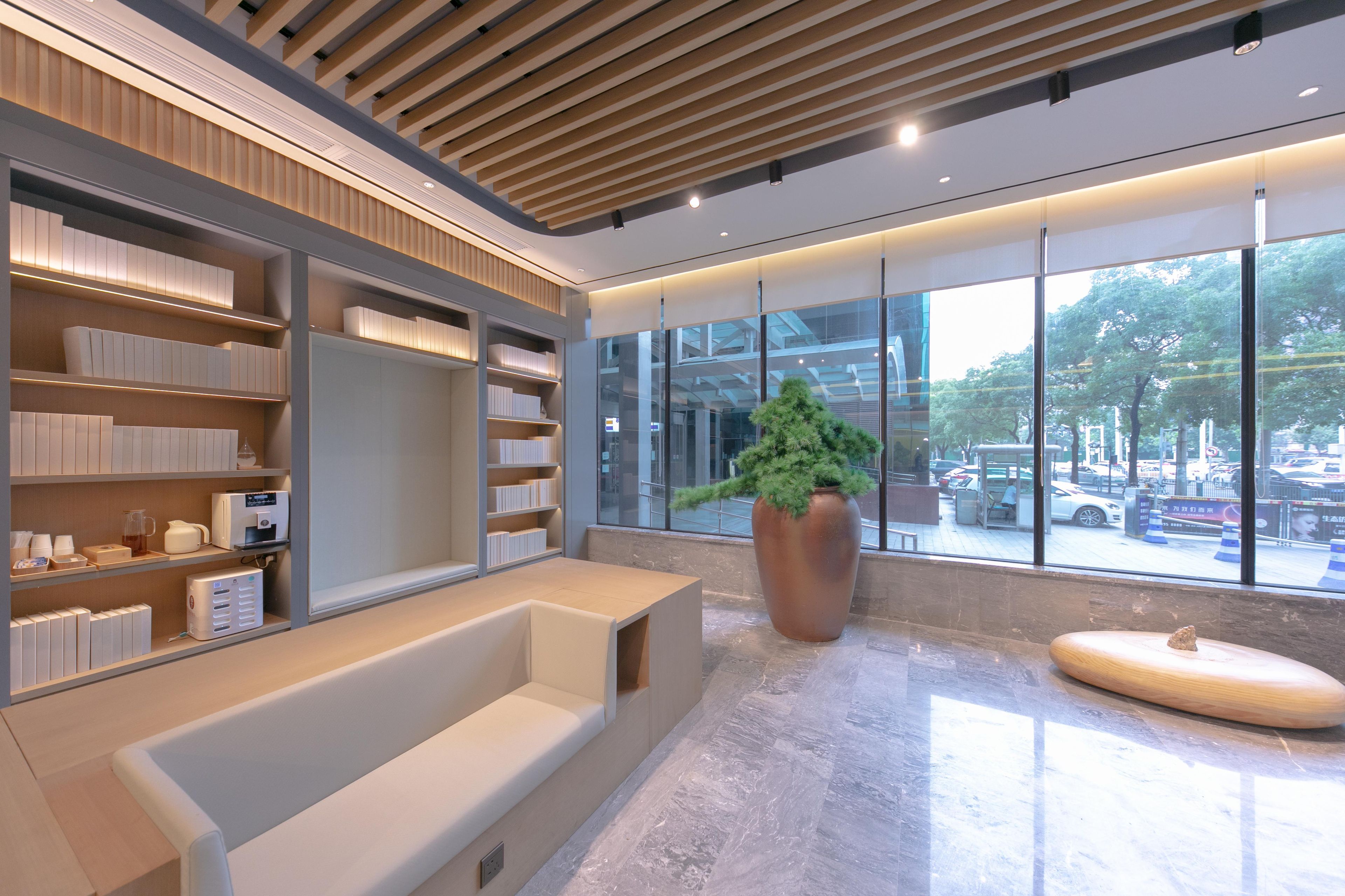 Un hall d’entrée moderne avec un espace salon, une grande plante en pot et une vue sur la rue grâce à de grandes fenêtres.
