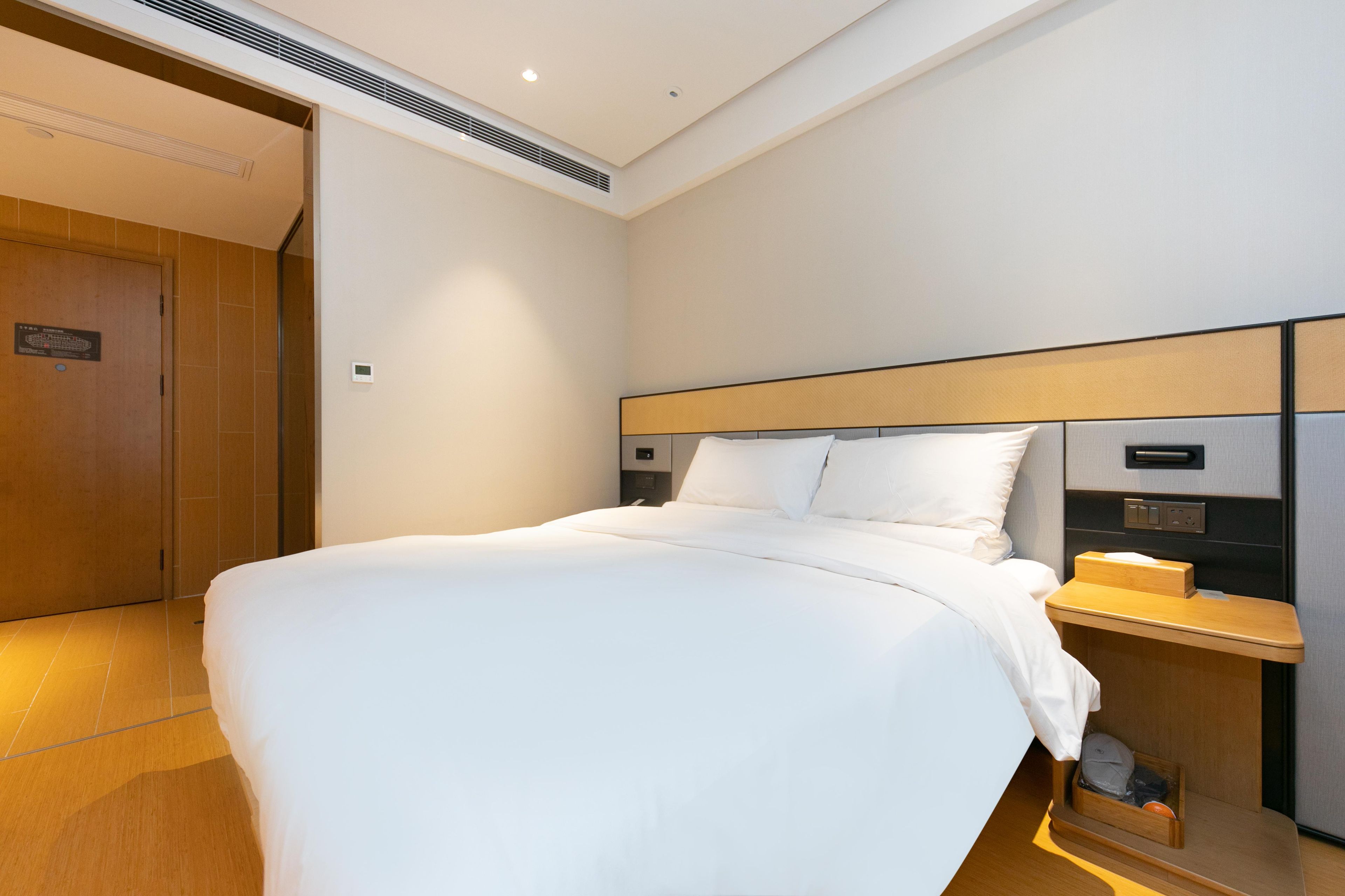 A hotel room with a large bed, a bedside table with a lamp, and a wooden door.