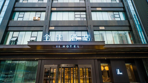 Et hotel med en moderne facade, store glasvinduer og en markant indgang med en roterende dør.