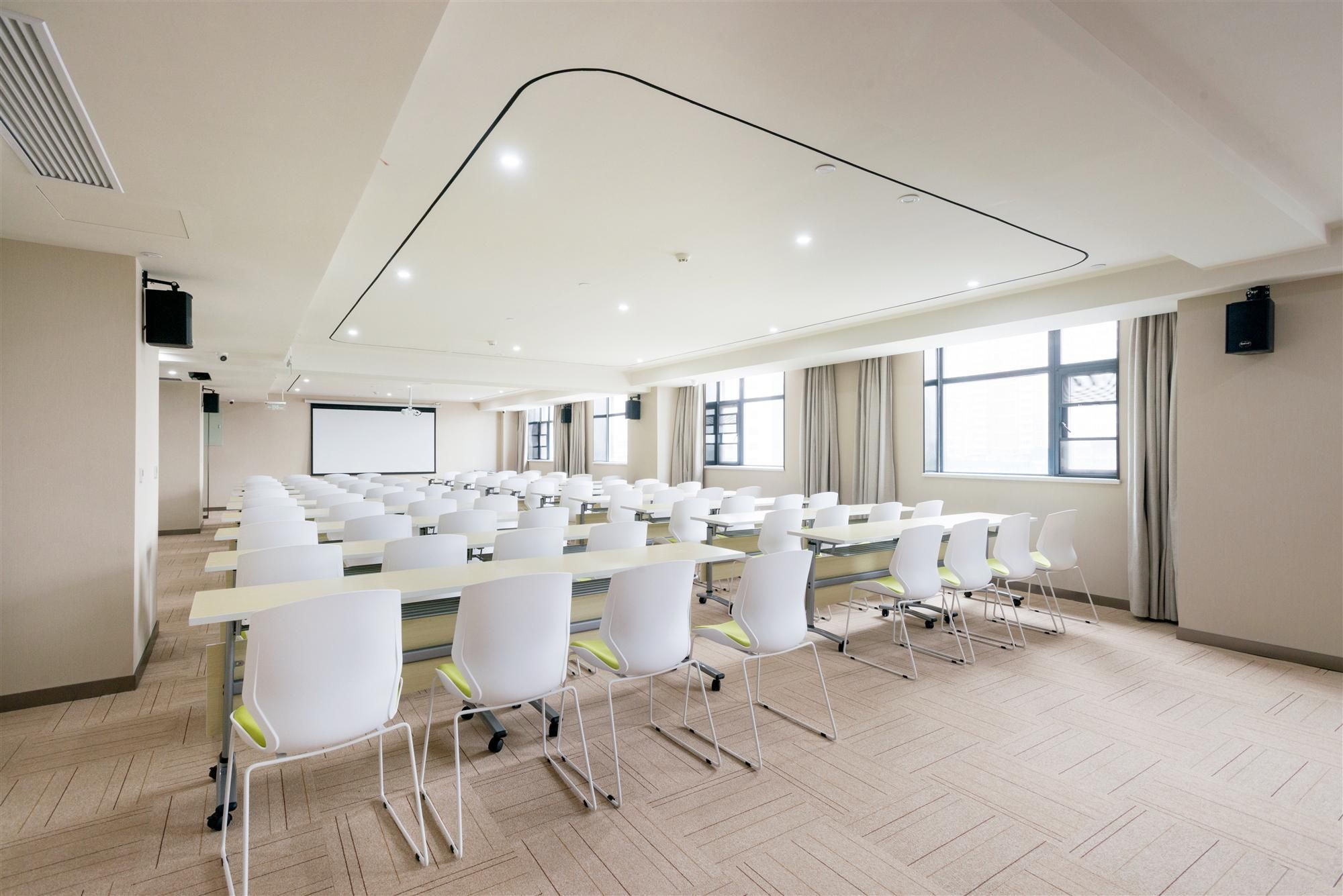 Une salle de conférence avec des rangées de chaises blanches, un grand écran et un projecteur.