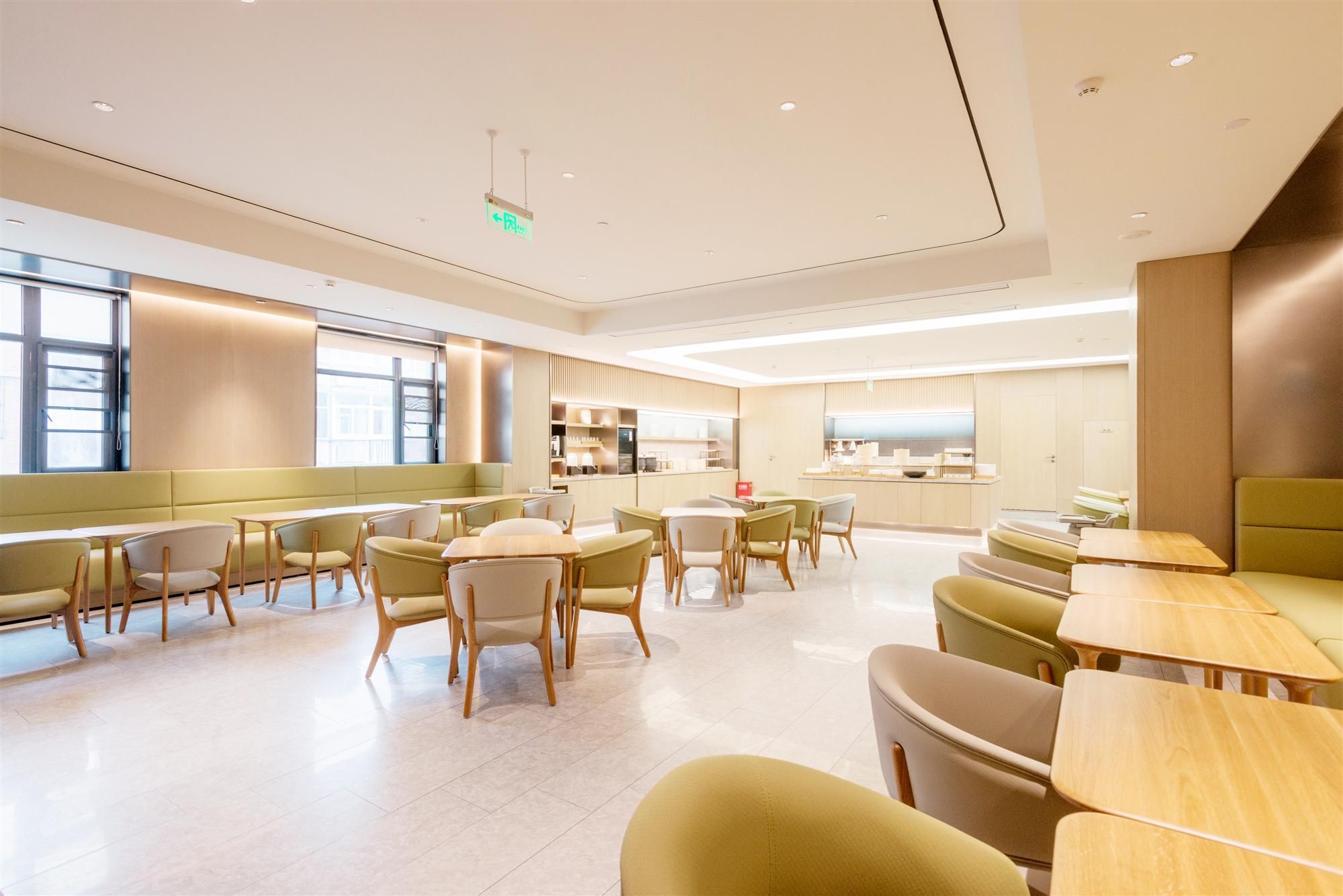 A modern dining area with multiple seating options, including tables and booths, and a kitchen area in the background.