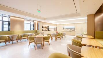 A modern dining area with multiple seating options, including tables and booths, and a kitchen area in the background.