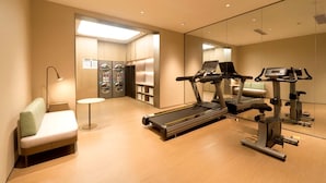 Et moderne fitnesscenter med løbebånd, motionscykel og et siddeområde med en lampe.