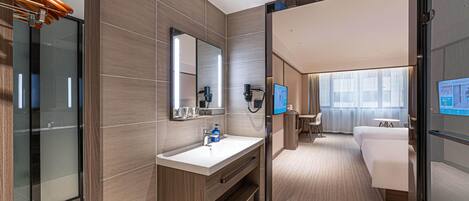 A modern hotel room with a large mirror, a sink, a hairdryer, a television, and a bed.