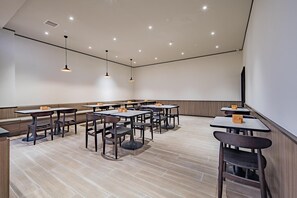 A modern dining area with multiple tables and booths, recessed ceiling lighting, and a large screen wall.