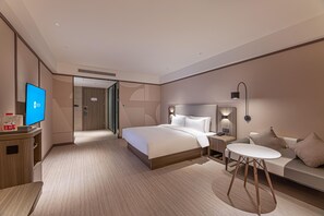 A modern hotel room with a large bed, bedside tables, a desk, a TV, and a seating area with a sofa and a small table. - Hanting Hotel (Chuzhou)